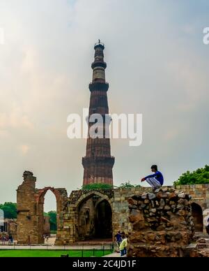 Qutub Minar, Delhi, India; 16-Aug-2019; a guy sitting on a wall with the Qutub Minar in the background Stock Photo