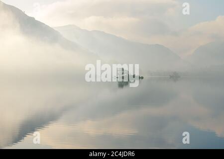 Isolated Island Reflected In A Calm Still Lake On A Peaceful Misty Summer Morning. Lake District, UK. Stock Photo
