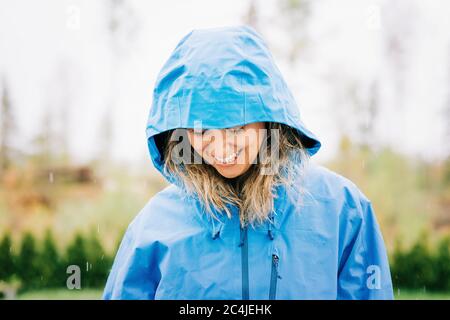 woman stood in the rain with a raincoat on smiling outside Stock Photo