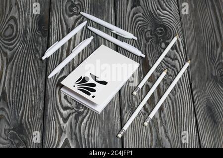 Notepad, white pencils and pens lie on pine boards painted in black and white. Stock Photo
