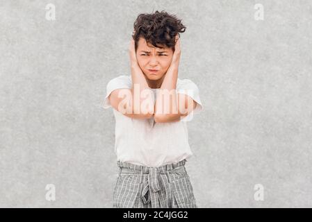 Young exhausted and stressed woman with creative hairstyle covering her ears with her hands. Don't want to hear anything or having headache. Stock Photo