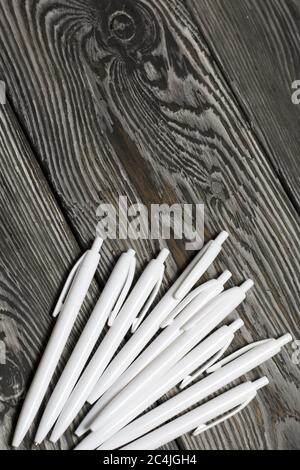 Several ballpoint pens in white. They lie on brushed pine boards painted in black and white. Stock Photo