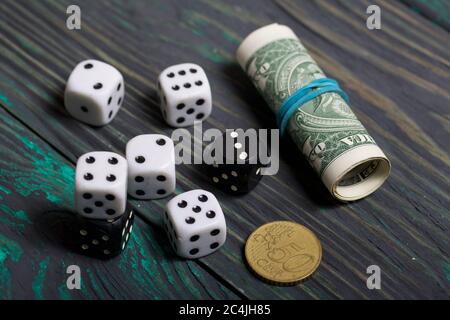 Dices are white and black. Nearby dollars rolled up into a tube and a coin. On brushed pine boards. Stock Photo