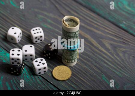 Dices are white and black. Nearby dollars rolled up into a tube and a coin. On brushed pine boards. Stock Photo