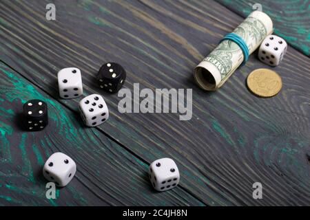 Dices are white and black. Nearby dollars rolled up into a tube and a coin. On brushed pine boards. Stock Photo