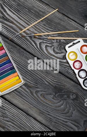 Watercolor for painting and brushes. Box with pastel. They lie on pine boards painted with white and black paint. Stock Photo