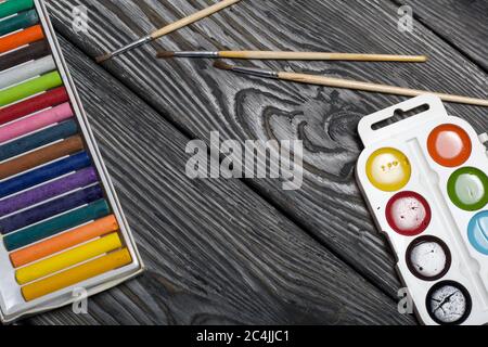 Watercolor for painting and brushes. Box with pastel. They lie on pine boards painted with white and black paint. Stock Photo