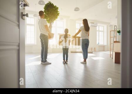 Happy family with children moving with boxes in a new apartment house. Back view. Stock Photo