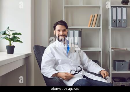 Portrait of smiling male doctor in medical office. Sitting comfortable in armchair, looking at camera. Stock Photo