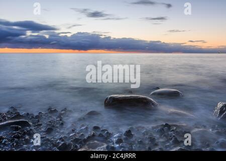 Baltic Sea on the island of Ruegen in the morning with sunrise. Dramatic clouds over the red colored horizon on the stony coastline. Large stones in t Stock Photo