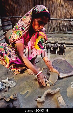 A woman works on earthen pots and vases. Colourful earthenware like pots, jars and vases enhance the beauty of city households. Besides, it is a sourc Stock Photo