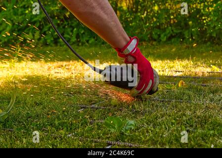 Cutting metal net with grinder on green grass. Sparks from contact materials. Worker outside, cut the steel net. Process with angle grinder. Stock Photo