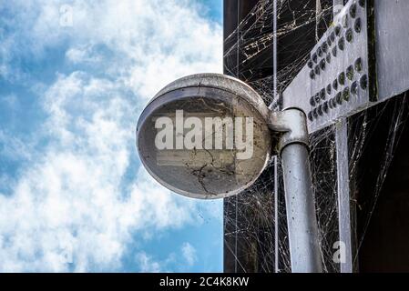 Spider web on a public street lamp attached to a steel railway bridge, with a blue sky with white clouds in the background. Stock Photo