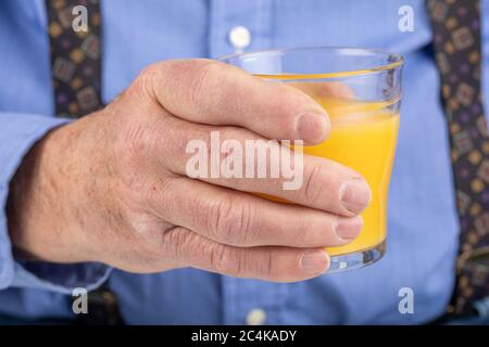 the rough hands of an elderly male holding a glass of orange juice Stock Photo