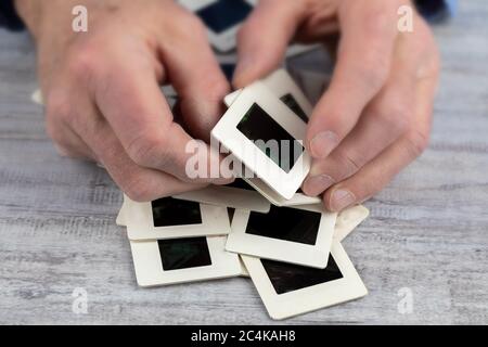 an elderly man hands sorting a pile of  35 mm slides of old photographs in his rough hands suggesting memory loss Stock Photo