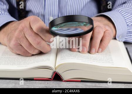 close up view of an elderly man using a magnifying glass to read a book Stock Photo