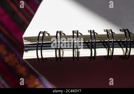 Sketchbook placed with the spiral binding up partly in the shade on colorful surface Stock Photo