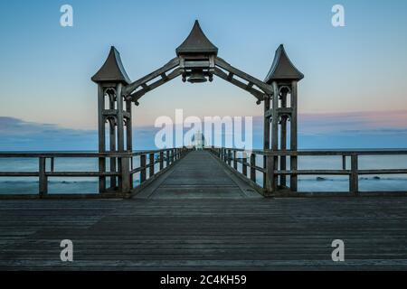 Pier on the Baltic Sea in the evening. Sunset with clouds on the horizon. Unlit wooden footbridge with wooden arch and bell on the island of Ruegen