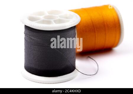 close up of a spool of black sewing thread with a spool of orange lying on its side isolated on white Stock Photo