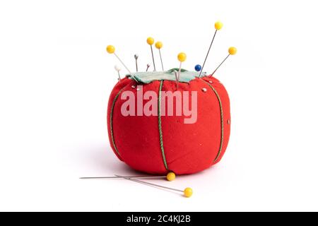 close up of a red pin cushion full of  straight pins and yellow quilt pins isolated on white Stock Photo