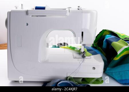 a white electric sewing machine sewing a seam on a home made covid-19 mask with scissors and spools of thread isolated on white Stock Photo