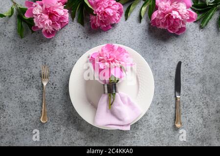 Elegance table setting with pink peony, white dishware, silverware on gray. Top view. Stock Photo