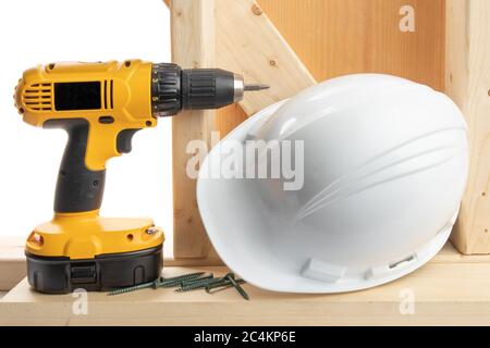 a yellow battery operated drill with screwdriver bit and a hard hat in a residential construction setting isolated on white Stock Photo