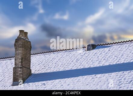 Snow-covered slate roof with old chimney Stock Photo