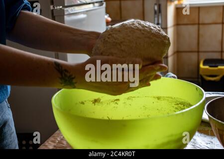 Female kneading the dough on a light green plastic bowl in the kitchen Stock Photo