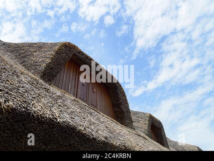 Traditional rural thatched house with brown windows, clear summer sky and some white clouds. Stock Photo