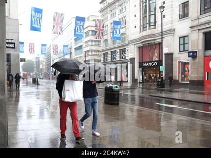 London, UK. 27th June, 2020. Two people shelter beneath their umbrellas during a rain shower in a very quiet Oxford Street in London. Credit: Paul Marriott/Alamy Live News Stock Photo