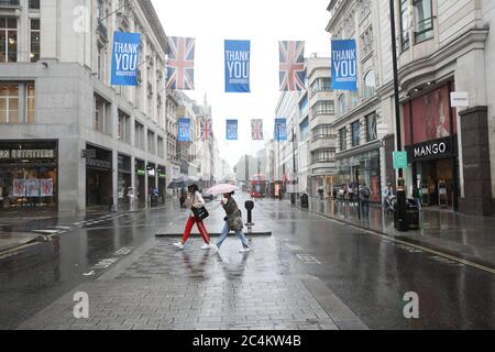 London, UK. 27th June, 2020. Two ladies shelter beneath their umbrellas during a rain shower in a very quiet Oxford Street in London. Credit: Paul Marriott/Alamy Live News Stock Photo