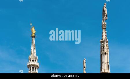 Milan Cathedral spires, Italy. Golden statue of Madonna and other sculptures on blue sky background. Famous Gothic Milan Cathedral or Duomo di Milano Stock Photo