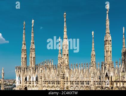 Milan Cathedral roof, Italy. Famous Milan Cathedral or Duomo di Milano is a top landmark of Milan. Luxury Gothic spires with statues on blue sky backg Stock Photo