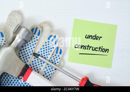 Repairman working tools with a sticker and an inscription on it under construction on a white wooden background. Stock Photo