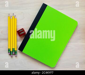 back to school - 4 yellow pencils, a red pencil sharpener and a green notebook on a wood desk with copy space Stock Photo