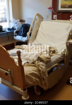 Empty unoccuppied hospital bed with unmade sheets and blankets Stock Photo