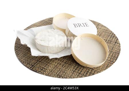 an unwrapped round of brie cheese on a rattan mat isolated on white Stock Photo