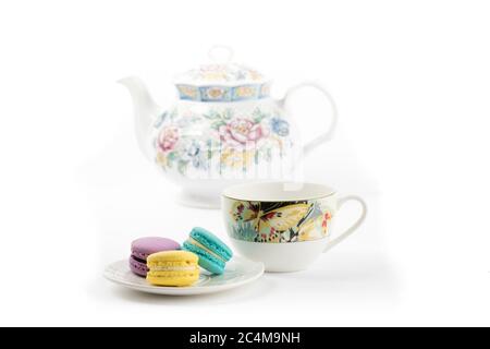 a plate of colorful meringue cookies with a teacup and a teapot on a white background Stock Photo