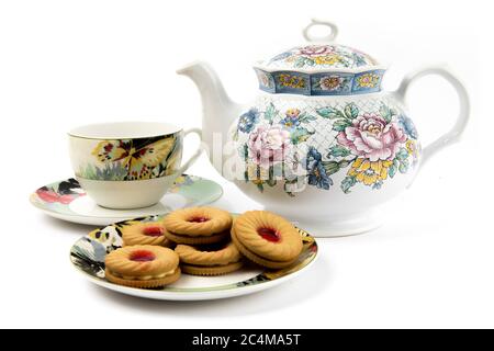 a plate of fruit cream cookies and a colorful teapot and tea cup on a white background Stock Photo