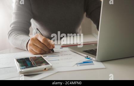 Business documents on table with smart phone and laptop computer and woman working in the background, Concept of finance economy, banking business and Stock Photo