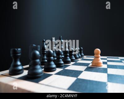 A single white chess pawn piece standing alone on a chessboard against a full team. Conceptual photo of an impossible fight and overcoming the enemy. Stock Photo