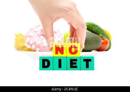 Female hand holding wooden text blocks spelling NO DIET in front of a plate with vegetables and donuts. Isolated on white, focus on the foreground. No Stock Photo