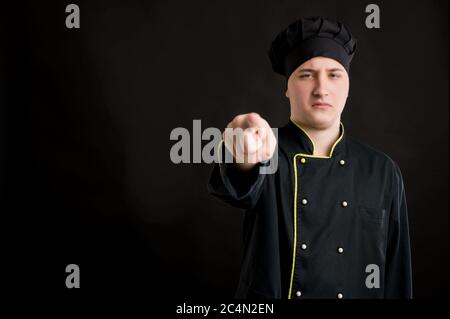 Young male dressed in a black chef suit pointing his finger posing on a black isolated background with copy space advertising area Stock Photo