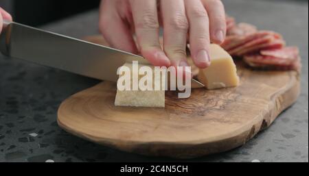 man slicing parmesan hard cheese on olive wood board Stock Photo