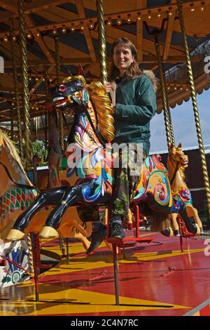 Lady on the Victorian horses carousel, gallopers, at Bressingham Steam & Gardens, Bressingham, Suffolk, UK Stock Photo