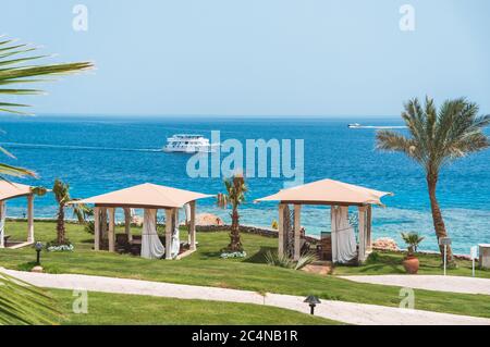 Seascape of turquoise sea with white boats and luxurious spa tents on green lawn near beach Stock Photo