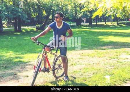 Young Indian man on bicycle with his smartphone in the park Stock Photo