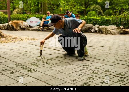 An old man writes calligraphy using a water brush in Shanghai’s Lu Xun Park. Stock Photo