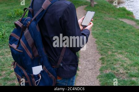 Man holding and using smartphone with blank white screen charges from the power bank in outdoor with nature background Stock Photo